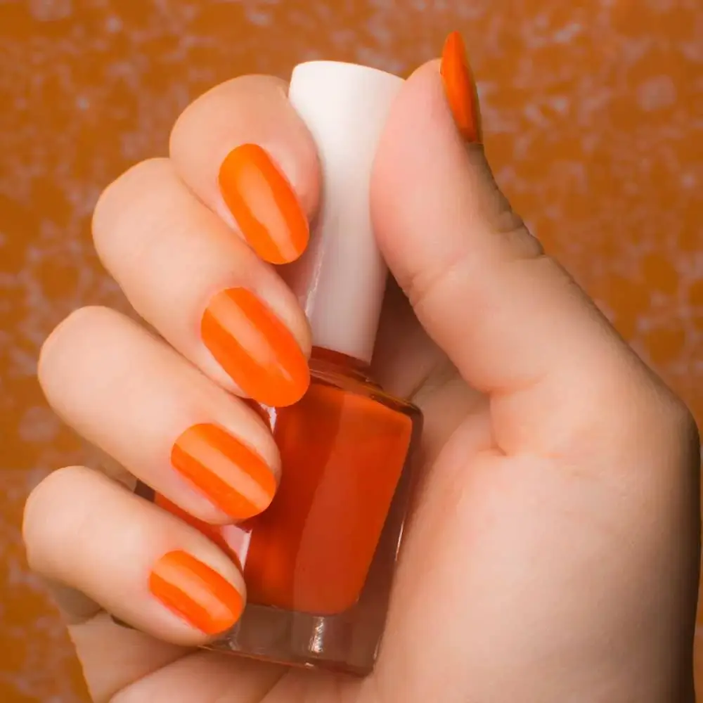 right hand with orange-colored nails and holding an orange nail polish