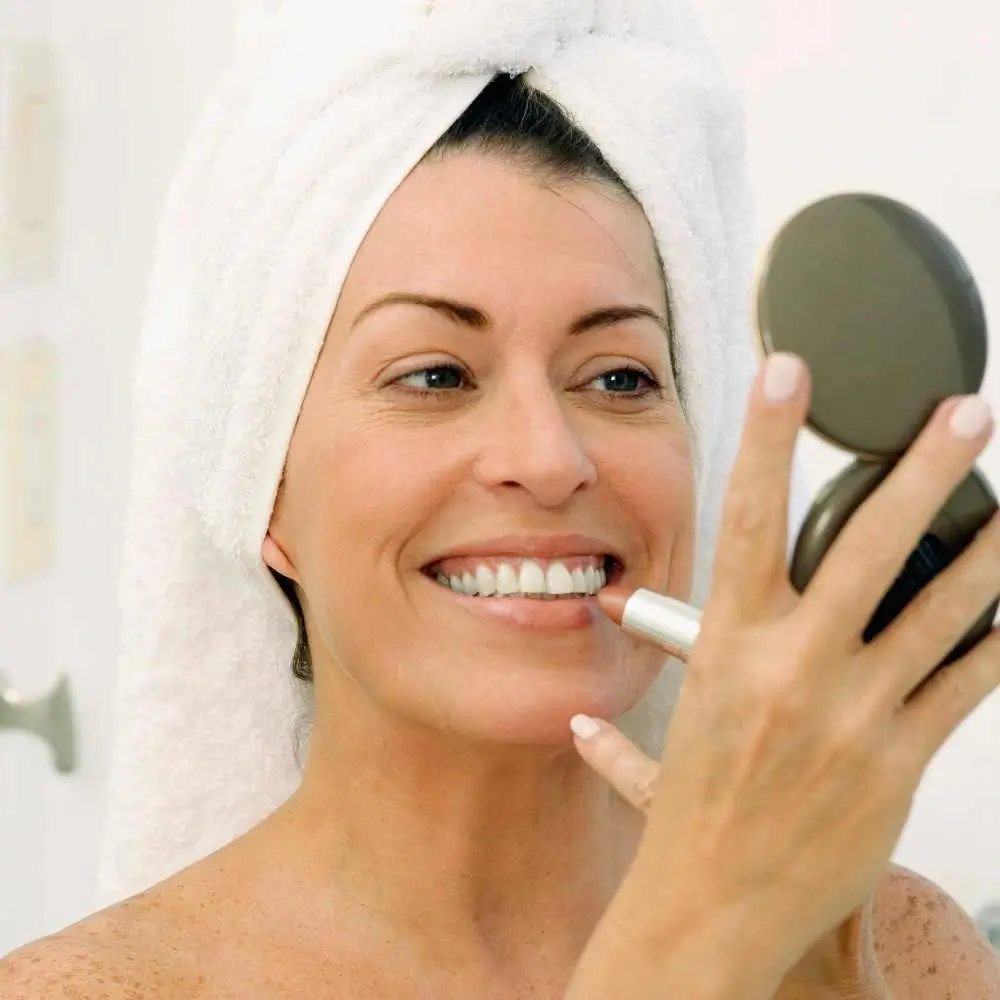 woman with a towel wrapped around her head applying nude lipstick