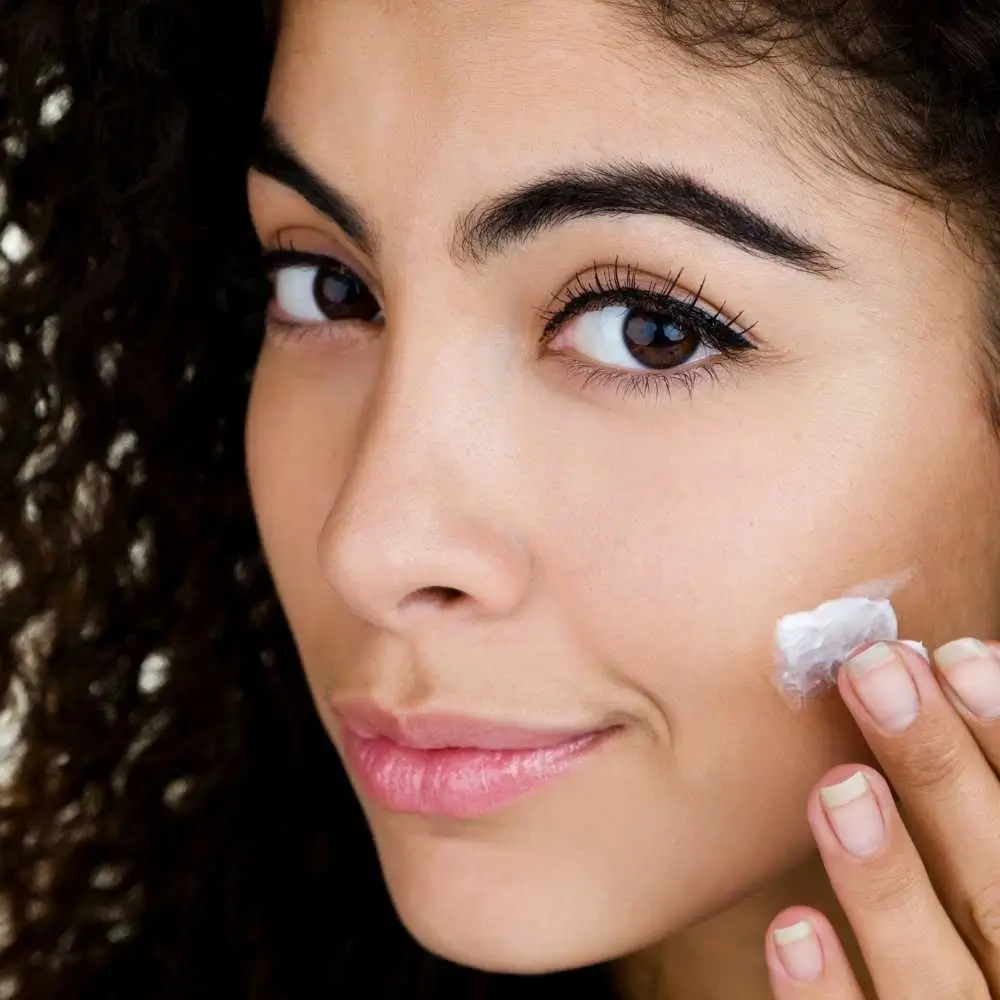 closeup portrait of a woman with curly hair applying moisturizer on her face