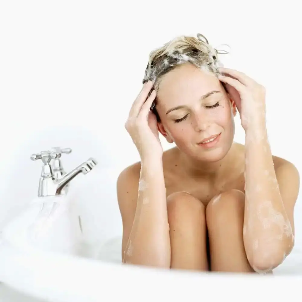young woman in the bath tub shampooing her hair